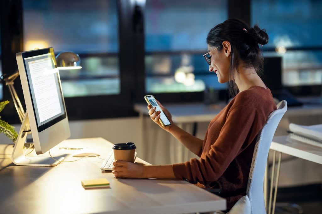 Beauty business woman having videocall with mobile phone while working with computer in the office.